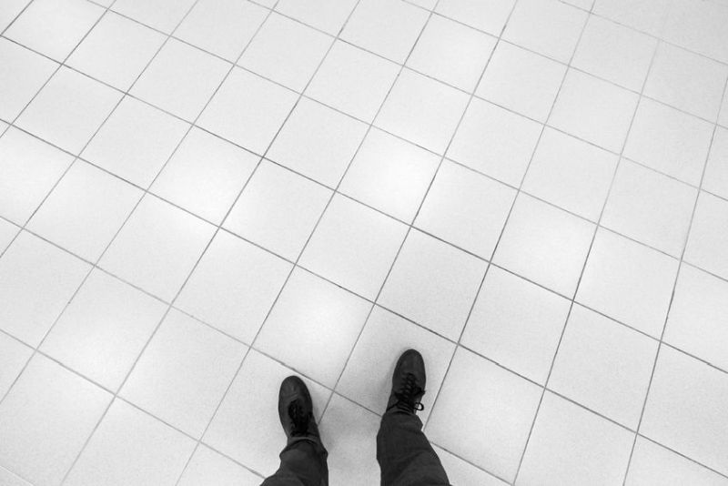 40869404 - male feet stand on office floor with white shining square tiling